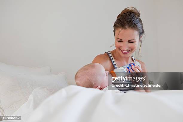 smiling mother bottle feeding baby - bottle milk baby stock-fotos und bilder