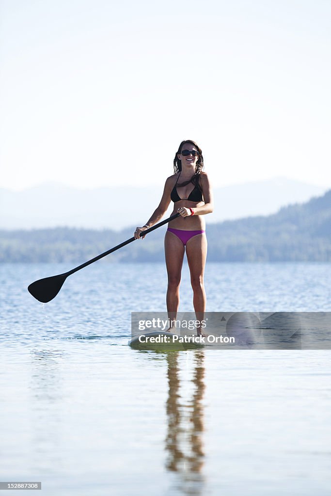 A athletic women smiling on a sunny day while stand up paddle boarding on a lake in Idaho.