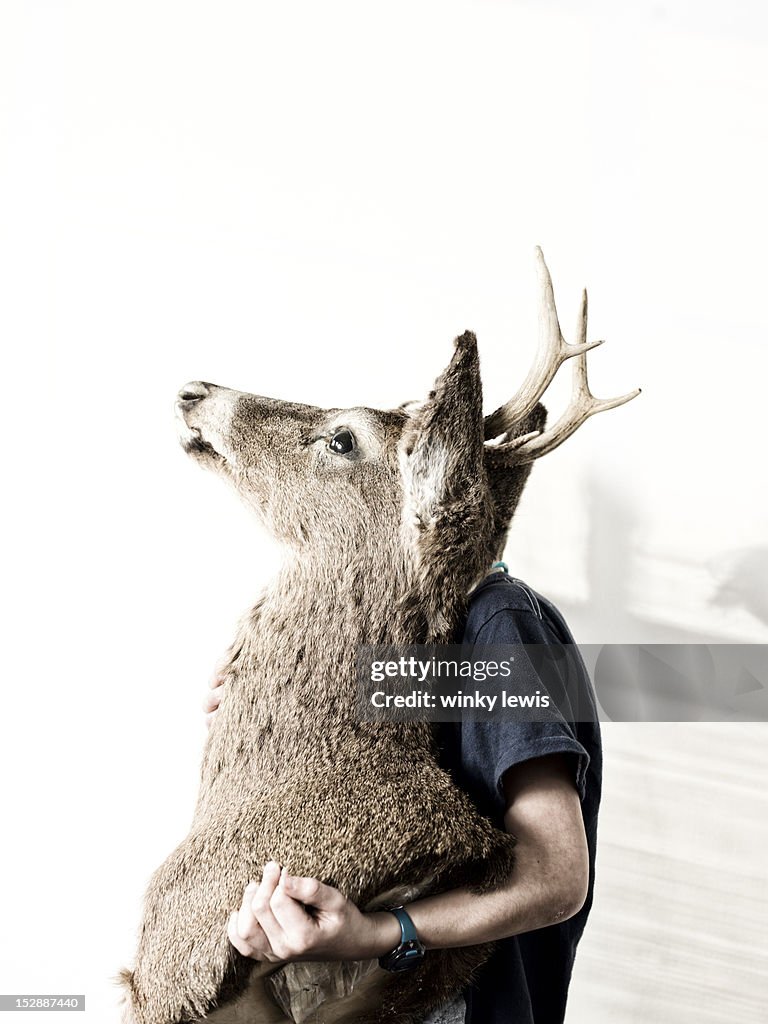 A boy sits holding a deer head