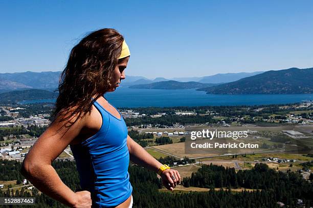 a happy athletic woman hiking stops and looks at her watch overlooking a lake in idaho. - pend orielle lake stock pictures, royalty-free photos & images