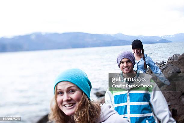 a group of three young adults smile while hiking at the edge of a lake in idaho. - pend orielle lake stock pictures, royalty-free photos & images