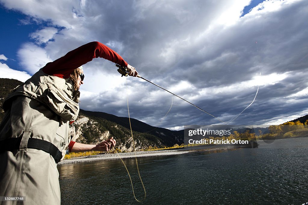 A fly fisher casting his line out of a boat while fly fishing surrounded by fall colors in Montana.