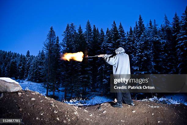 a young man shooting a large gun with a flame coming out of the barrel in montana. - montana western usa 個照片及圖片檔