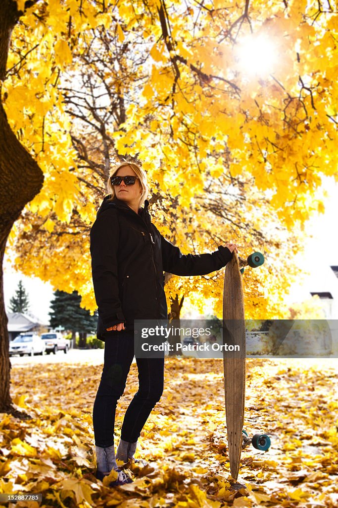 A athletic woman holding her skateboard surrounded by fall colors in Montana.