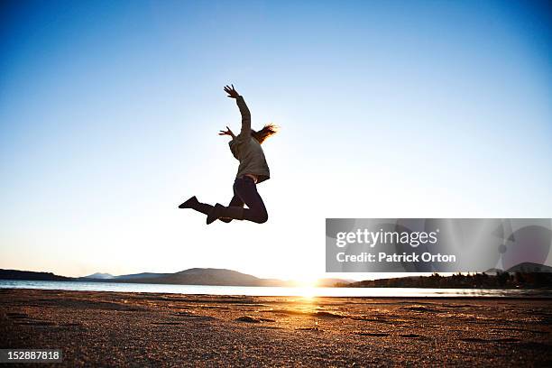 a athletic young woman leaping into the air at sunset next to a lake in idaho. - pend orielle lake stock pictures, royalty-free photos & images