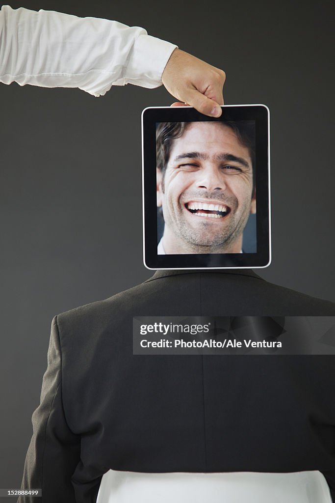 Man concealed behind Digital tablet displaying image of laughing man, rear view