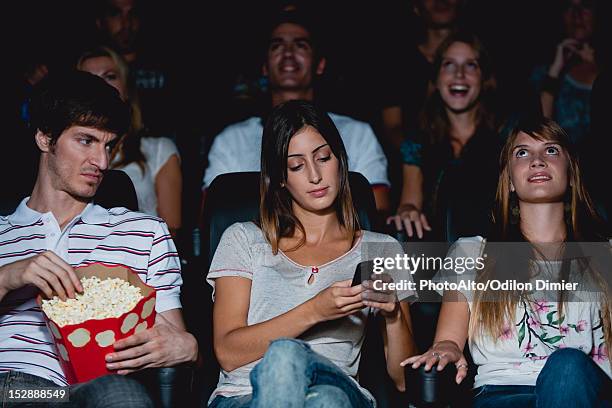 woman using cell phone in movie theater, man looking over with annoyed expression - antisocial stockfoto's en -beelden