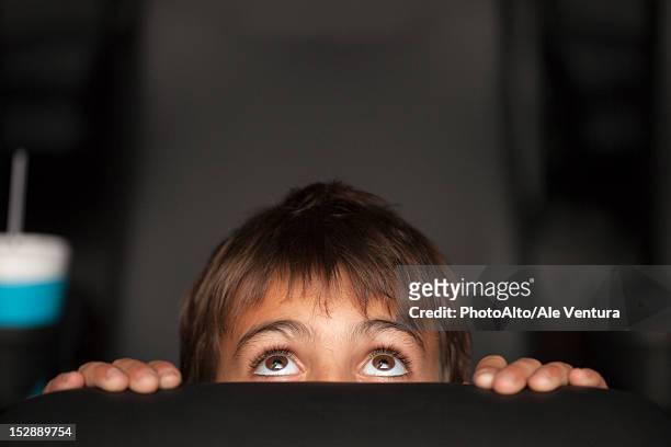 boy peeking over top of seat during horror movie in theater - scared boy imagens e fotografias de stock