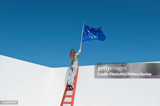 businesswoman standing at top of ladder, holding european union flag - europe flag stock pictures, royalty-free photos & images