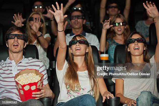 audience wearing 3-d glasses in movie theater, arms reaching out - 3d cinema stock pictures, royalty-free photos & images