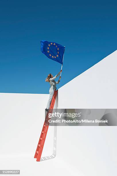 businesswoman standing at top of ladder, holding european union flag - european union flag stock-fotos und bilder