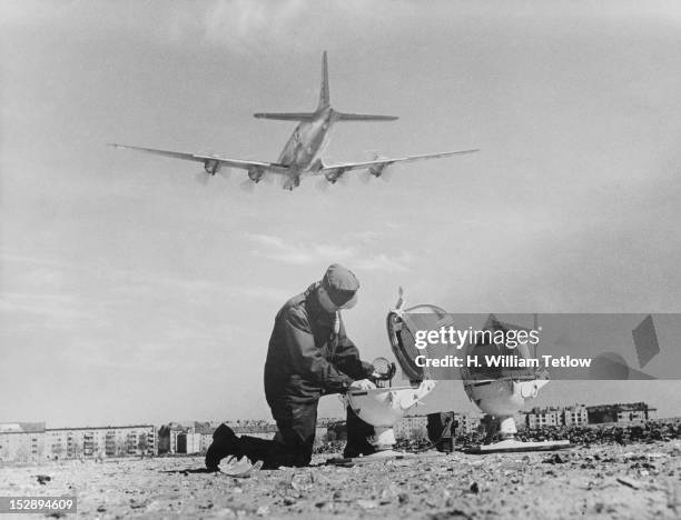 Technician mends the broken glass of a landing light at Tempelhof Airport in Berlin, during the Berlin Airlift, 25th April 1949. A Douglas C-54...