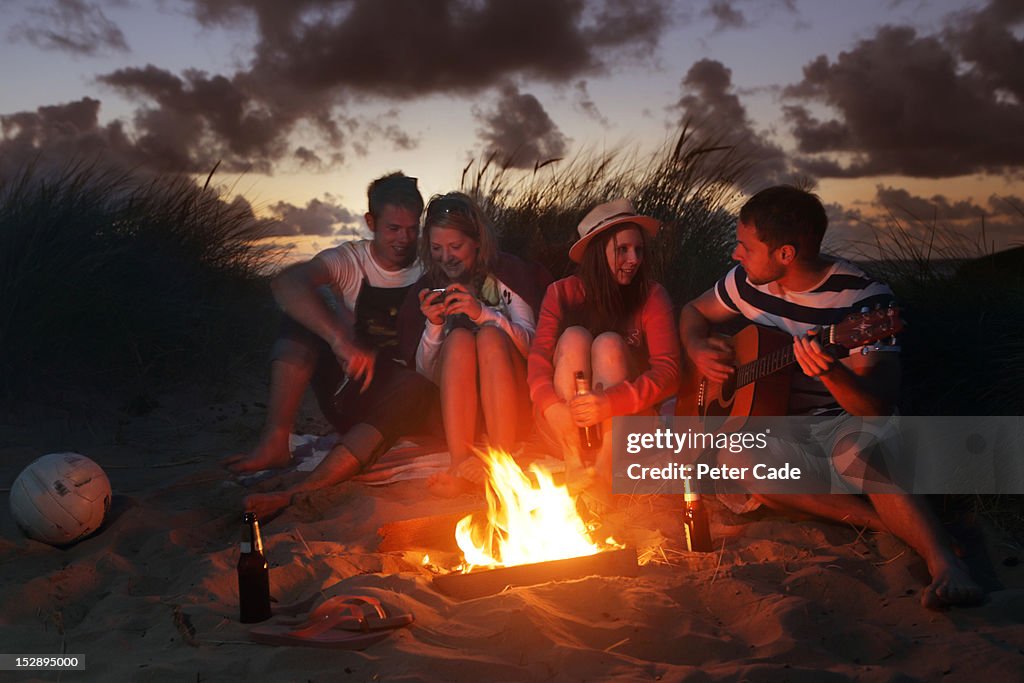 Young adults sat around fire in sand dunes