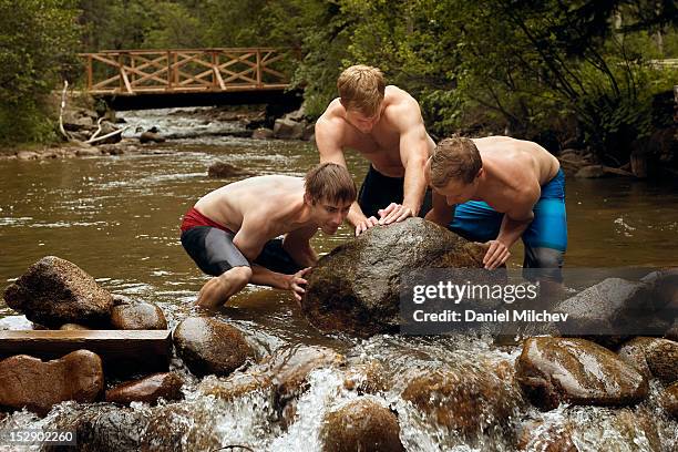 friends moving a rock in the river. - nur erwachsene stock-fotos und bilder