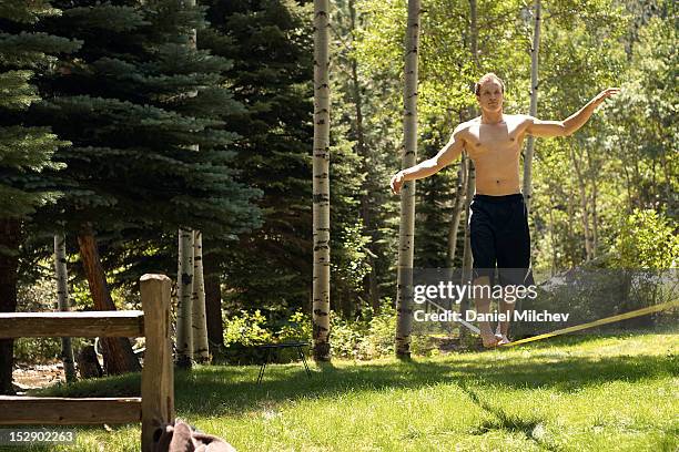 guy waking on a slack-line in the woods. - slackline foto e immagini stock