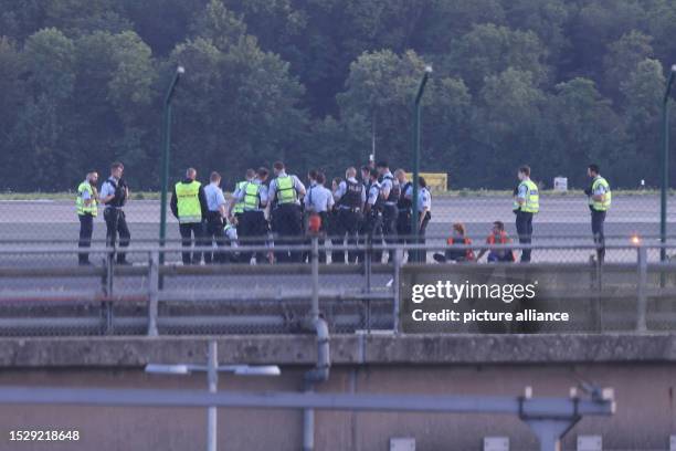 July 2023, North Rhine-Westphalia, Duesseldorf: Police officers stand on the airfield and try to detach activists of the group Last Generation from...