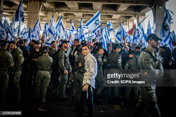An Ultra-orthodox Jewish youth looks back as he stands behind a line of border police officers facing protestors waving the Israeli flag during a...