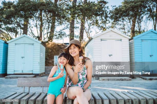 mom & daughter eating ice cream joyfully in front of the beach huts at beach - ice cream shop stock pictures, royalty-free photos & images