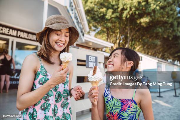 mom & daughter eating ice cream joyfully outside an ice cream parlour at the beach - family at beach stock pictures, royalty-free photos & images