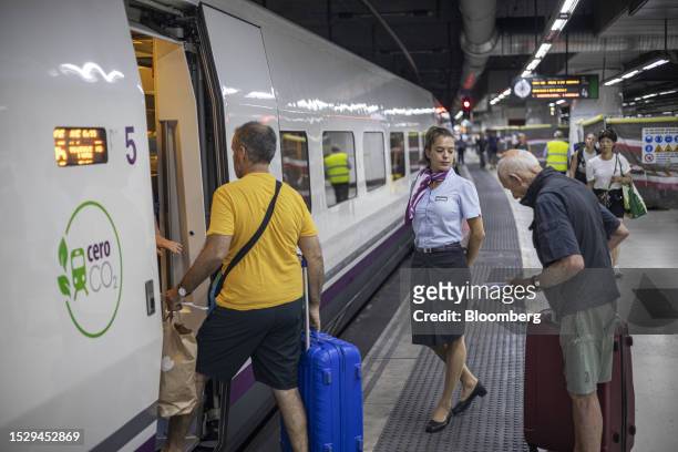 Worker helps passengers board the first Barcelona-Lyon train, operated by Renfe Operadora SC, at Sants railway station in Barcelona, Spain, on...