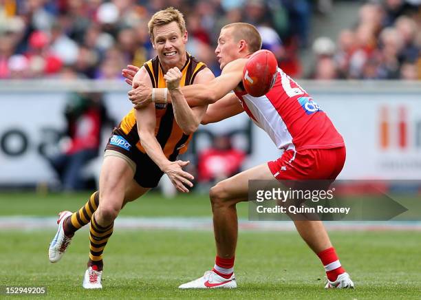 Sam Mitchell of the Hawks handballs whilst being tackled by Sam Reid of the Swans during the 2012 AFL Grand Final match between the Sydney Swans and...