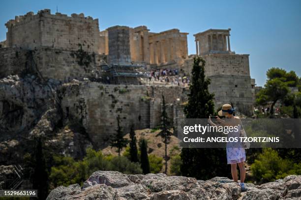 Woman takes a photograph of the Acropolis archaeological site in Athens on July 13 as Greece hits high temperatures. Greece's national weather...