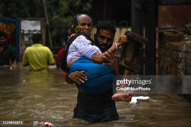 Man carries a woman as they wade through a flooded locality after the Yamuna River overflowed due to heavy rainfall in New Delhi, India on July 13,...