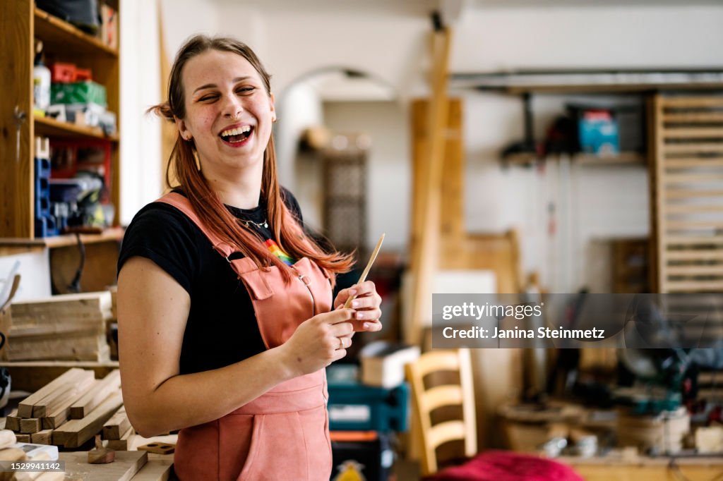 Young woman smiles into the camera while standing in a wood workshop
