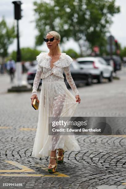 Guest wears black large cat eyes sunglasses, a white lace embroidered pattern / ruffled V-neck / long sleeves / long dress, a gold embossed striped...