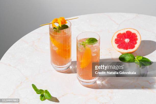 fresh summer cocktail with citrus. orange and grapefruit, mint with ice cubes. drinking glass of soda drink. cold lemonade recipe. two glasses - grapefruit cocktail stock pictures, royalty-free photos & images