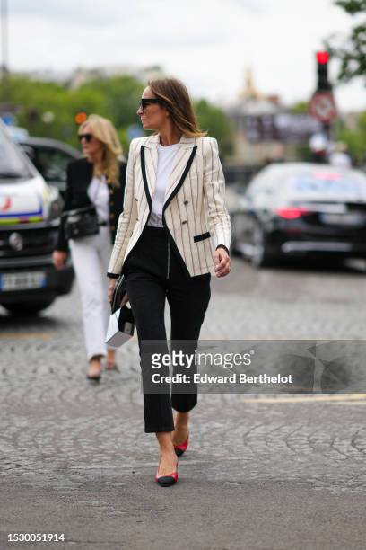 Guest wears black squared sunglasses, a white t-shirt, a white latte with black striped print pattern buttoned blazer jacket, black denim pants, a...
