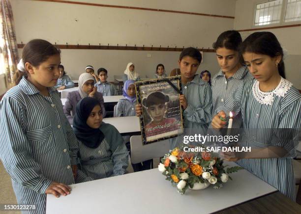 Palestinian pupils light a candle and place a bouquet of flowers at the desk of fellow pupil Riham Ward , slain two years ago by an Israeli tank...