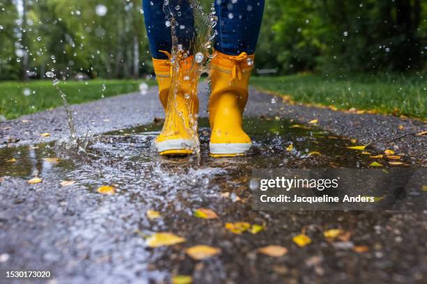 a person walks through a puddle on the sidewalk in fall - rubberlaars stockfoto's en -beelden