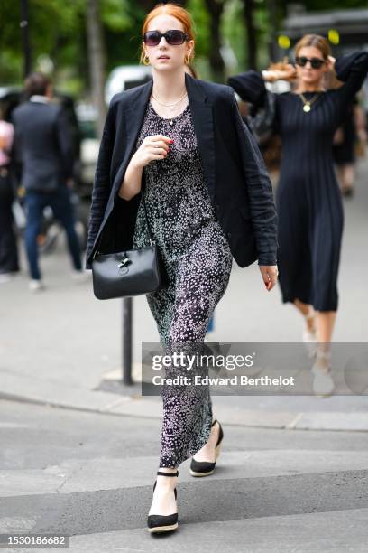 Guest wears black sunglasses, gold earrings, a black blazer jacket, a black and white print pattern long dress, a black shiny leather handbag from...