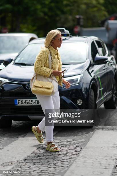 Guest wears pale orange circle sunglasses, a pale yellow fluffy tweed high neck jacket from Chanel, white denim large pants, a pale yellow matte...