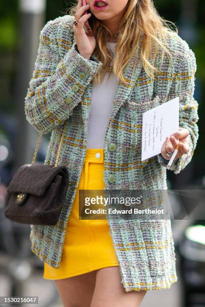 Guest wears a white t-shirt, a pale green and orange checkered print pattern tweed blazer jacket, a black fabric shoulder bag from Chanel, a yellow...