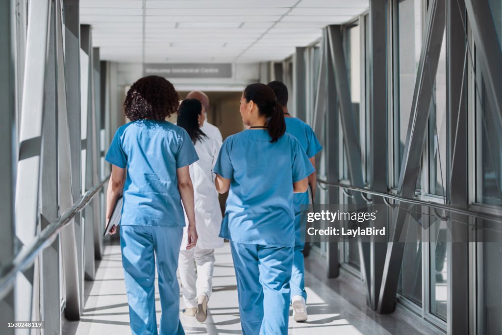 Vue arrière d’infirmières marchant avec des collègues dans le couloir de l’hôpital