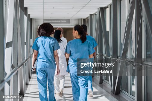Rear view of female nurses walking with coworkers in hospital corridor Rear view of female nurses walking with coworkers in hospital corridor