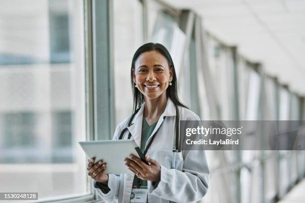 portrait of cheerful female doctor with digital tablet beside window in corridor - digital devices beside each other bildbanksfoton och bilder