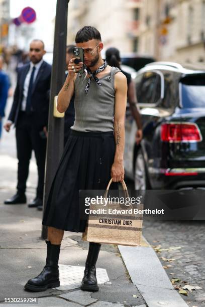 Guest wears glasses, silver rings, a black with white print pattern silk scarf, a gray ribbed wool tank-top, a gray ribbed tank-top, a black pleated...