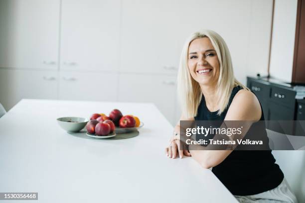 beautiful blond woman with charming smile sitting at table with fruit in dining room - camiseta de tirantes fotografías e imágenes de stock