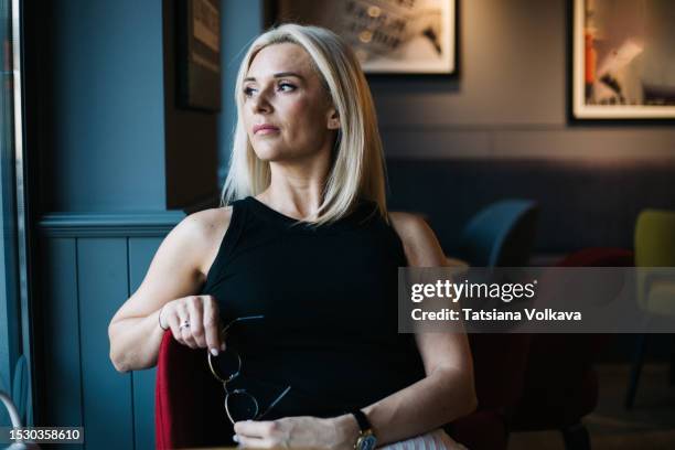 attractive lady in black top enjoys tranquil ambiance of restaurant sitting alone at table - ambiance girly stock pictures, royalty-free photos & images