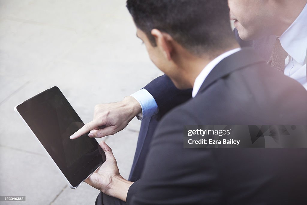 Two businessmen using a tablet outside.