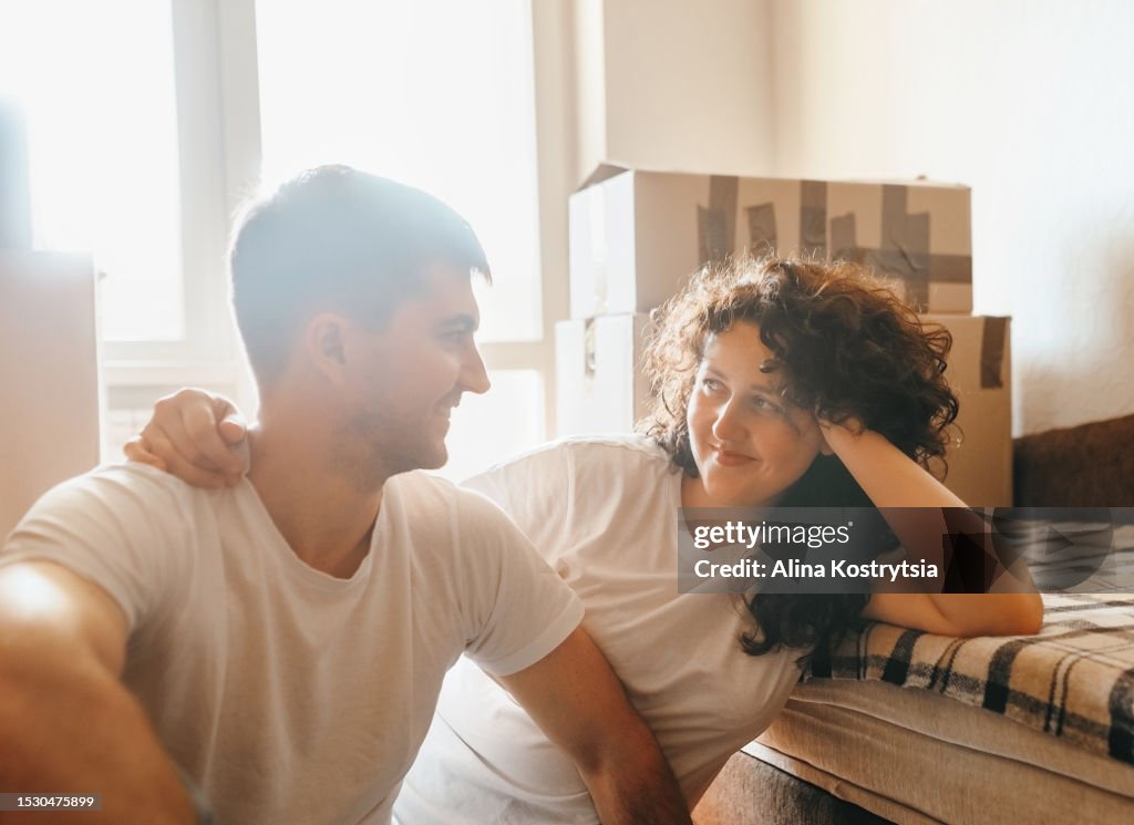 Joyful couple sitting on floor surrounded by paper boxes.