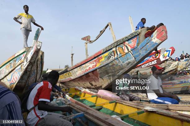 People stand and sit on dugouts parked on the beach at a fishing quay, in Mbour on July 13, 2023. Seeking a better life and employment, increasing...