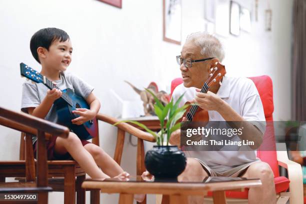 happy grandson sitting with grandfather singing while playing ukulele at home, cherishing moments of quality time and strengthening their family bond. - disruptaging stock pictures, royalty-free photos & images