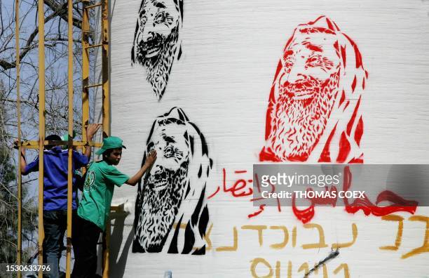 Palestinian kids climb along a water reservoir with paintings of Hamas late leader Sheikh Ahmed Yassin and Arabic writing reading "The victorious...