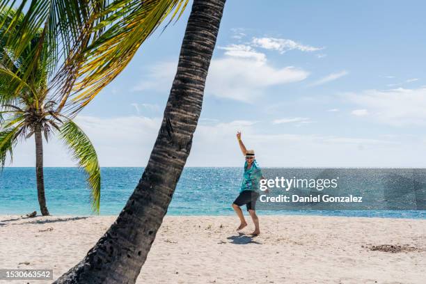 excited anonymous man dancing on beach near palms in sunlight with v sign - greater antilles stock pictures, royalty-free photos & images