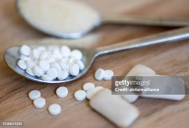 July 2023, Saxony, Leipzig: A spoonful of sweetener tablets lies next to a spoonful of sugar and chewing gum with sweeteners. A sweetener commonly...