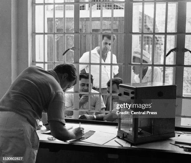 Group of men standing on the far side of a window buying diamonds as a man on the near side of the window writes beside a set of scales at the...